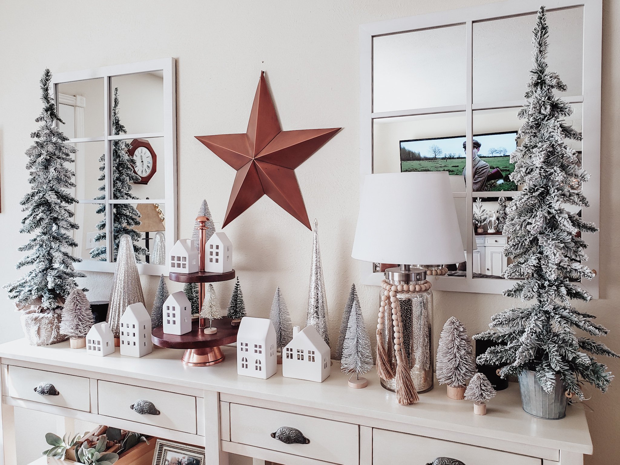 White Christmas village with white and silver bottle brushes. The village is flanked with 3' tall flocked artificial Christmas trees.