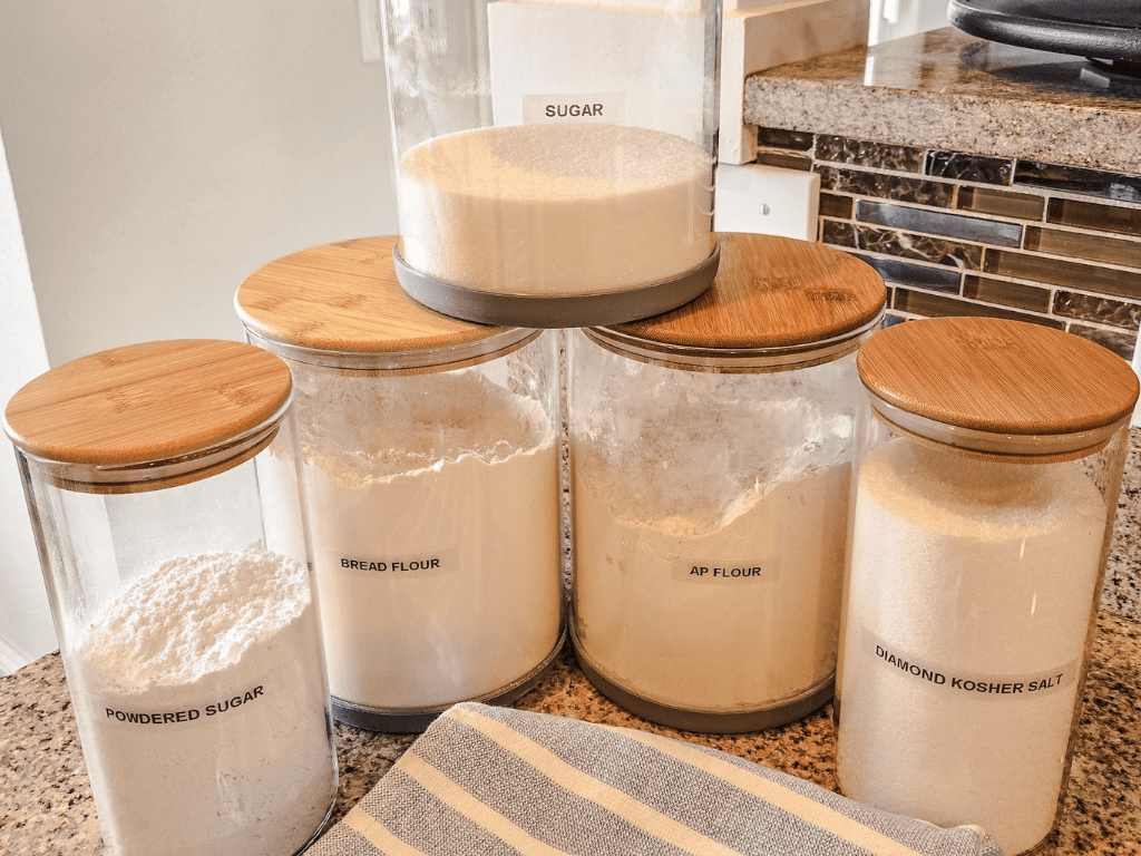 Glass jars with bamboo lids and labels filled with flour, sugar, salt.