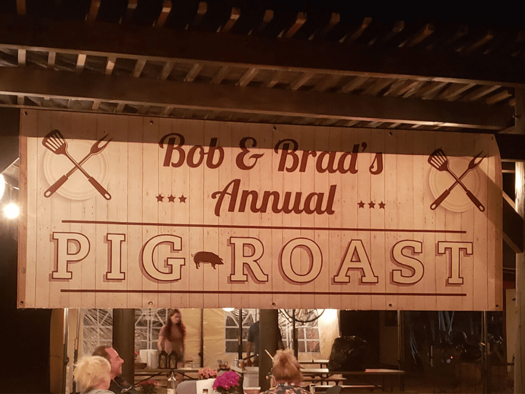 Pig Roast sign hanging from a wooden pergola.