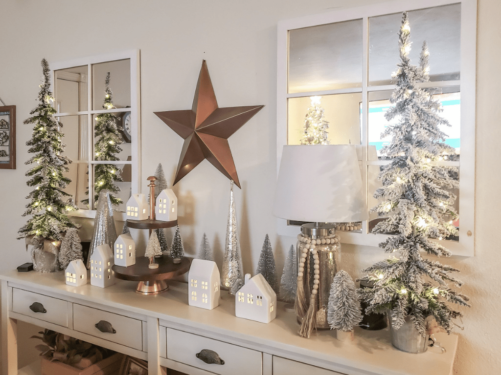 White Christmas village with white and silver bottle brushes. The village is flanked with 3' tall flocked artificial Christmas trees.
